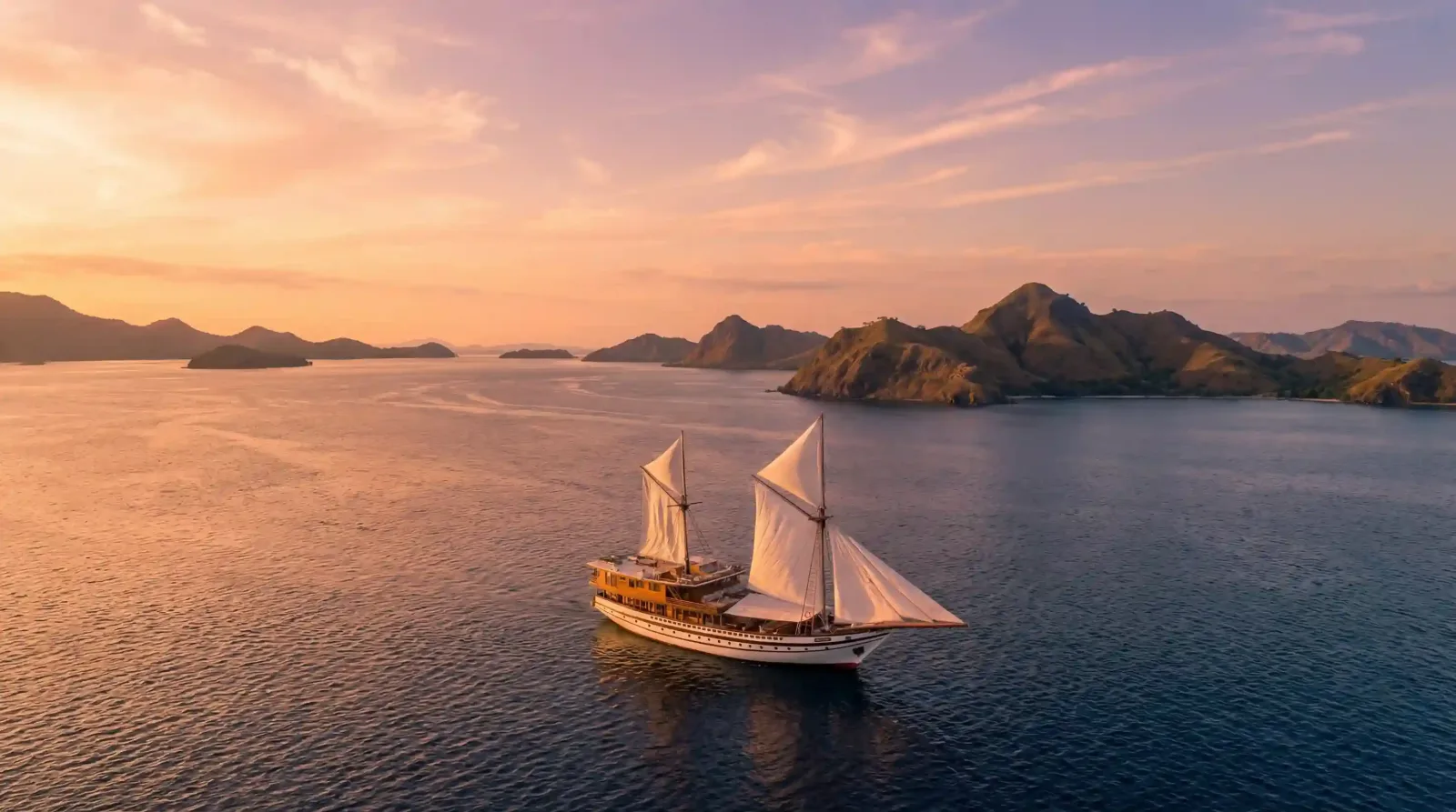 A phinisi sailing between islands at dawn