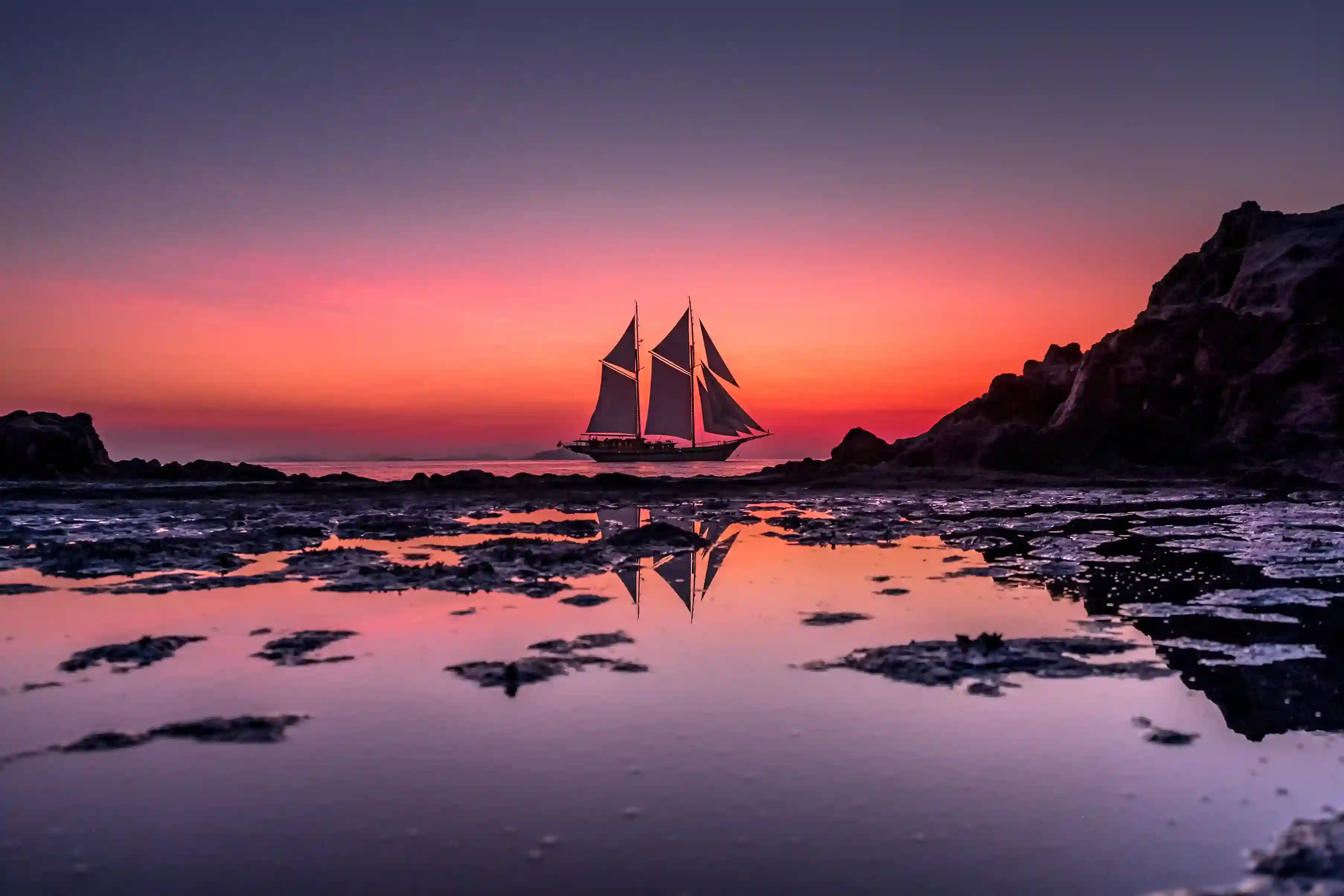 A phinisi under sail at sunset on open water